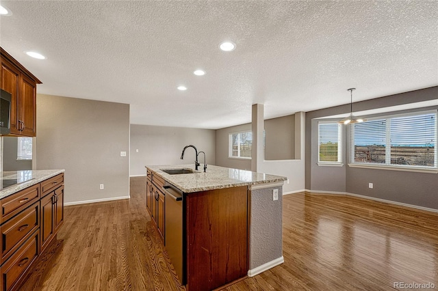 kitchen with a kitchen island with sink, dark wood-type flooring, sink, a textured ceiling, and decorative light fixtures