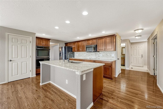 kitchen featuring a center island with sink, sink, dark hardwood / wood-style floors, appliances with stainless steel finishes, and tasteful backsplash