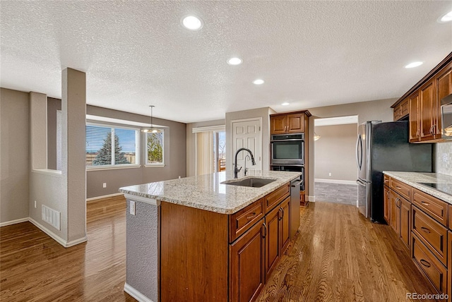 kitchen featuring a textured ceiling, sink, decorative light fixtures, a center island with sink, and hardwood / wood-style flooring