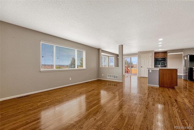 unfurnished living room with a textured ceiling, dark wood-type flooring, and sink