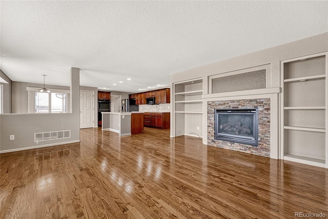 unfurnished living room with a fireplace, dark hardwood / wood-style flooring, a textured ceiling, and built in features