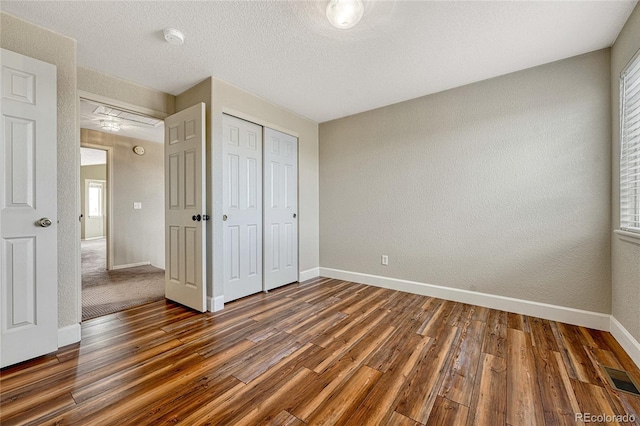 unfurnished bedroom featuring dark hardwood / wood-style floors, multiple windows, a textured ceiling, and a closet