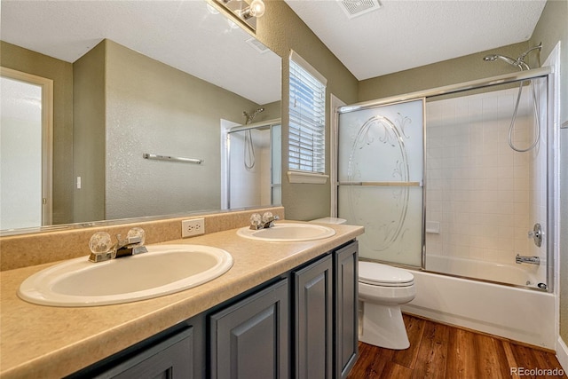 full bathroom with enclosed tub / shower combo, wood-type flooring, a textured ceiling, toilet, and vanity