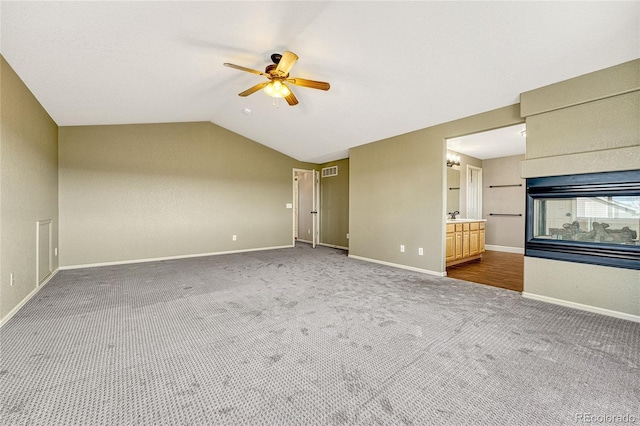 unfurnished living room featuring a multi sided fireplace, carpet floors, vaulted ceiling, and ceiling fan