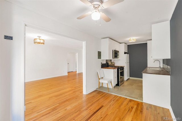 kitchen with a sink, white cabinetry, stainless steel appliances, light wood finished floors, and ceiling fan