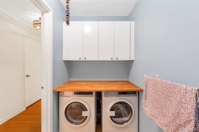 clothes washing area with cabinet space, light wood finished floors, and washing machine and clothes dryer