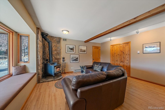 living room featuring visible vents, baseboards, light wood-style floors, beamed ceiling, and a wood stove