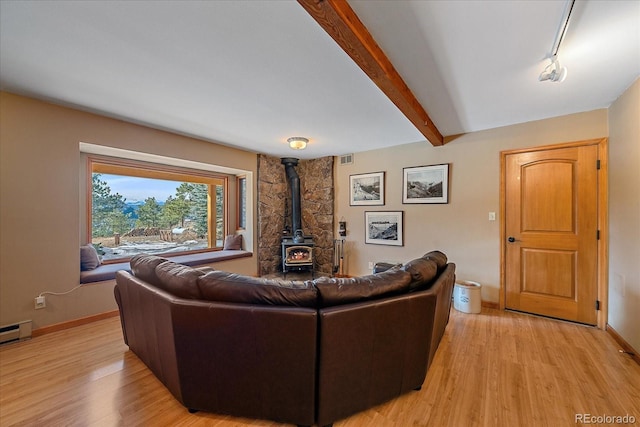 living room with light wood finished floors, beam ceiling, a wood stove, and baseboards