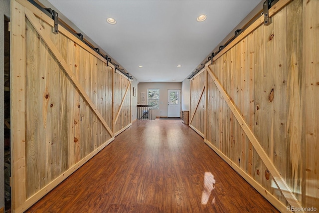 interior space with a barn door, wood walls, wood finished floors, and recessed lighting