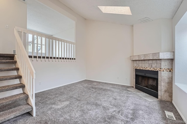 unfurnished living room with carpet flooring, a textured ceiling, a tile fireplace, and a skylight