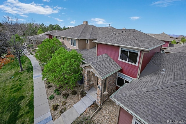 view of property exterior featuring roof with shingles, a residential view, a chimney, and stone siding