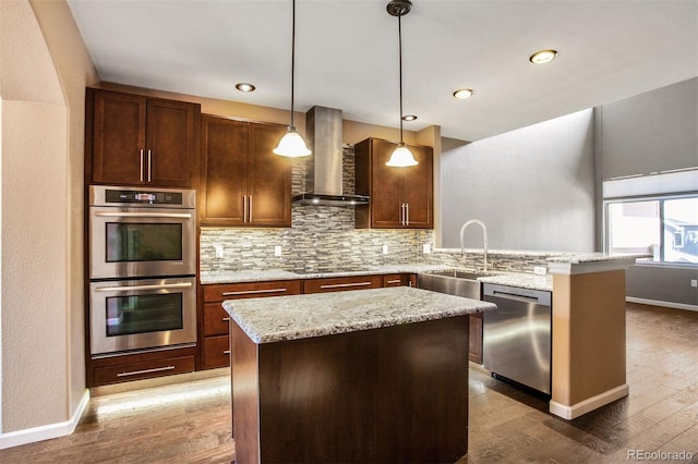 kitchen with appliances with stainless steel finishes, a sink, wall chimney exhaust hood, a peninsula, and backsplash