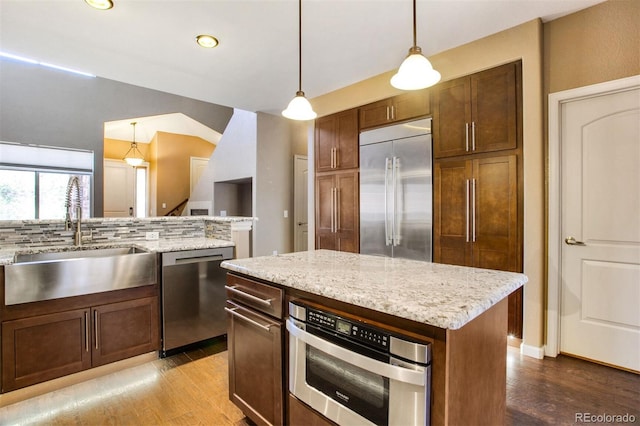 kitchen featuring decorative backsplash, wood finished floors, a sink, appliances with stainless steel finishes, and hanging light fixtures