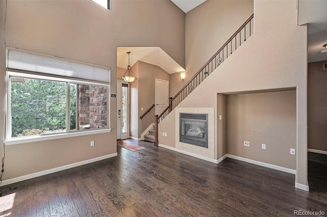 unfurnished living room featuring stairs, wood finished floors, baseboards, a high ceiling, and a tile fireplace