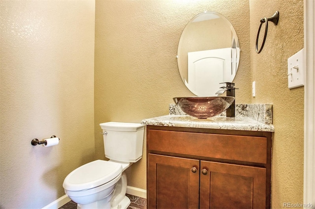 half bathroom featuring vanity, baseboards, a textured wall, and toilet