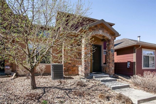 view of front of property featuring central AC, a shingled roof, and stone siding