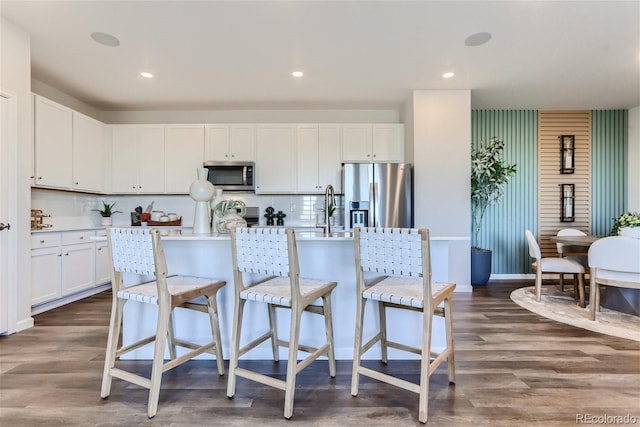 14133 Deertrack Ln, Parker, CO 80134 - kitchen featuring stainless steel appliances, dark wood-style floors, a kitchen island with sink, decorative backsplash, and a breakfast bar area