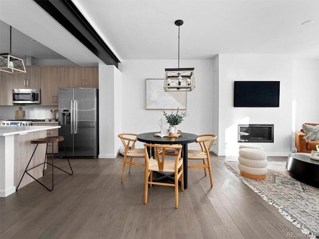 dining space featuring baseboards, wood finished floors, and a glass covered fireplace