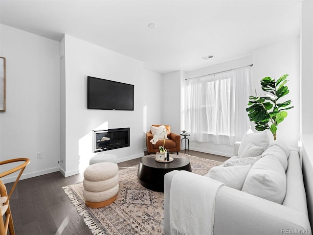living area with dark wood-type flooring, baseboards, and a glass covered fireplace