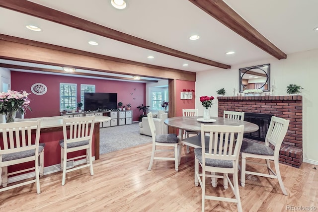 dining area featuring a fireplace, beamed ceiling, and light hardwood / wood-style floors