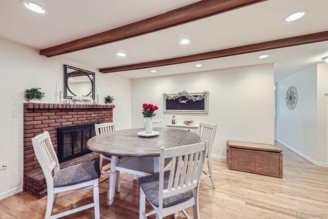 dining space featuring beam ceiling, a brick fireplace, and hardwood / wood-style floors