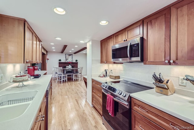 kitchen with backsplash, sink, stainless steel appliances, and light hardwood / wood-style floors