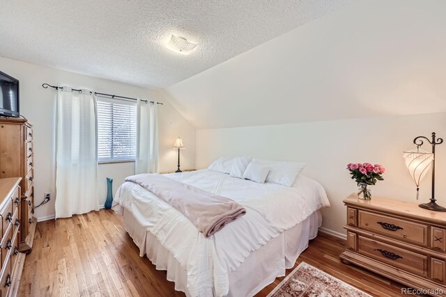 bedroom with a textured ceiling, lofted ceiling, and hardwood / wood-style floors