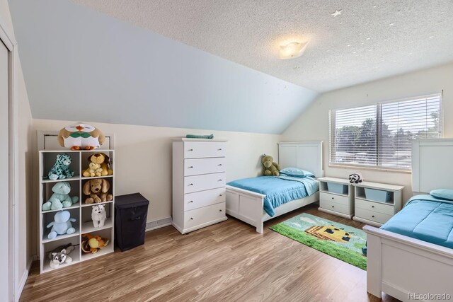 bedroom featuring light hardwood / wood-style flooring, a textured ceiling, and lofted ceiling