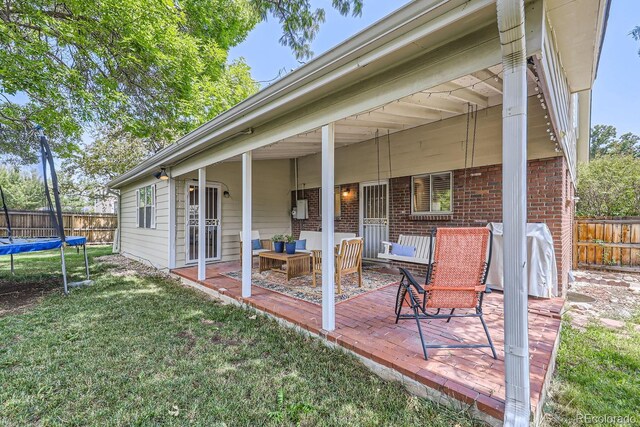 rear view of property featuring outdoor lounge area, a patio area, a lawn, and a trampoline