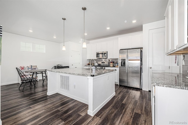 kitchen with pendant lighting, white cabinetry, stainless steel appliances, dark wood-type flooring, and a center island with sink