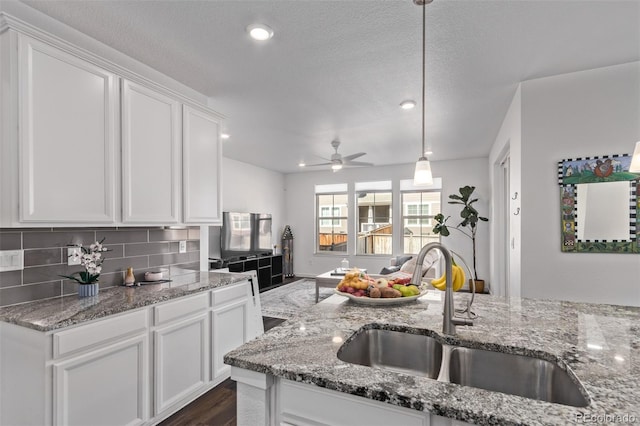 kitchen with a sink, a ceiling fan, white cabinets, backsplash, and light stone countertops