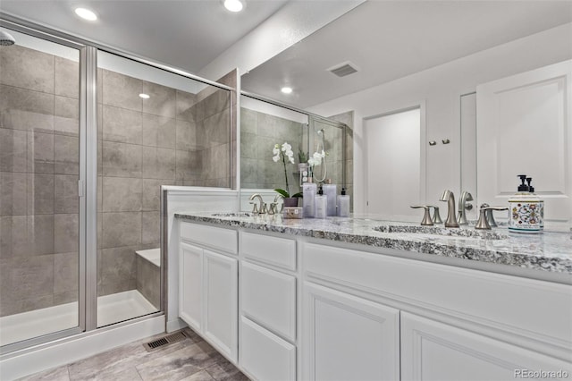 full bath featuring double vanity, a shower stall, visible vents, and a sink