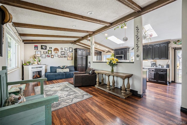 living room featuring a lit fireplace, a healthy amount of sunlight, vaulted ceiling with skylight, and wood finished floors