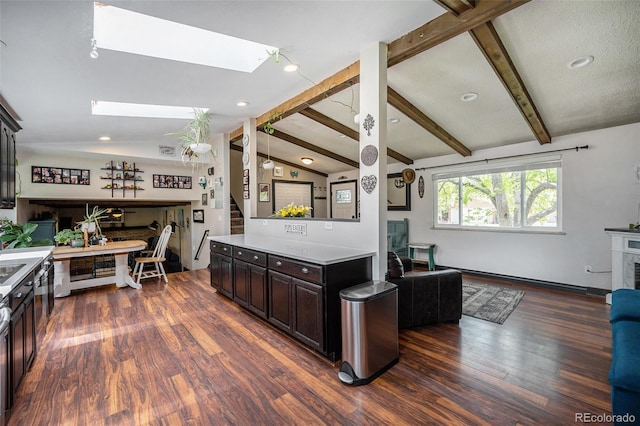 kitchen with dark brown cabinets, vaulted ceiling with skylight, light countertops, open floor plan, and dark wood-type flooring
