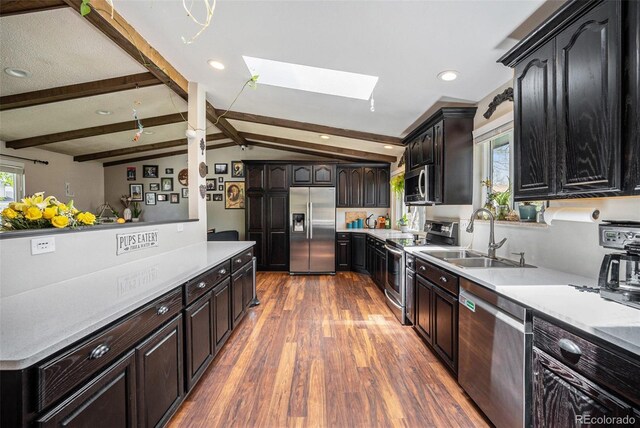 kitchen with vaulted ceiling with skylight, wood finished floors, a sink, light countertops, and stainless steel appliances