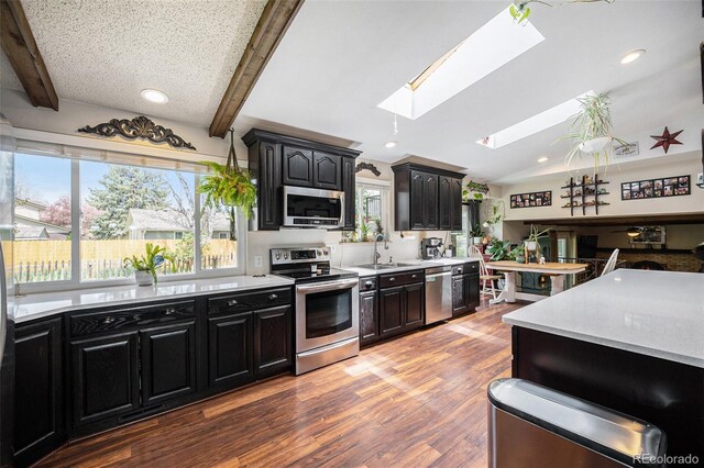 kitchen with appliances with stainless steel finishes, a sink, light countertops, dark cabinets, and wood finished floors