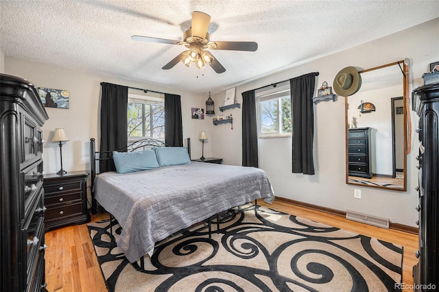 bedroom with a ceiling fan, a textured ceiling, visible vents, and light wood-type flooring