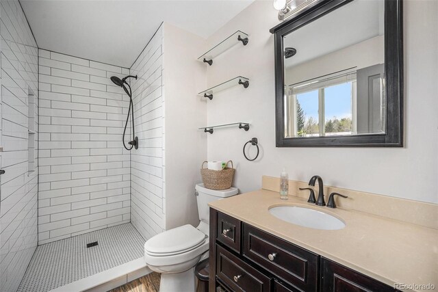 bathroom with vanity, wood finished floors, a tile shower, and toilet