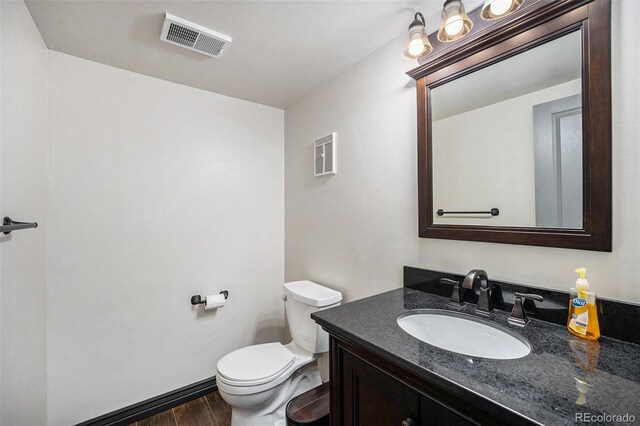 half bath with toilet, visible vents, wood finished floors, and vanity