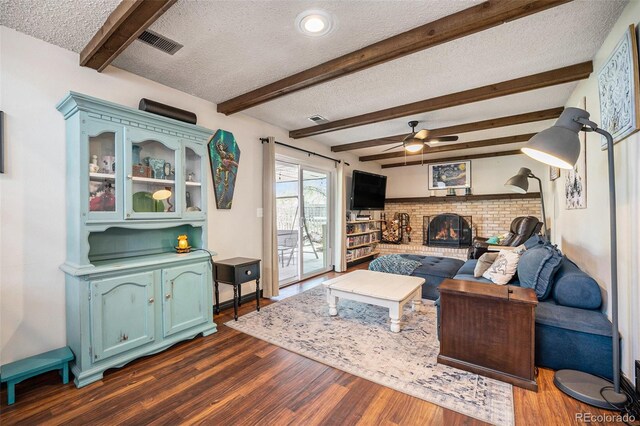 living room with visible vents, dark wood-style flooring, a fireplace, a textured ceiling, and a ceiling fan