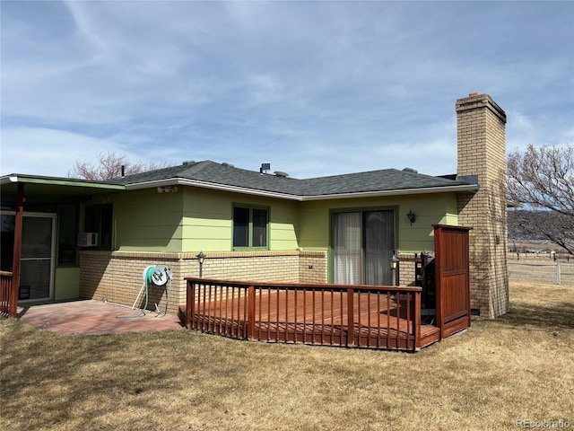 back of property with a lawn, a shingled roof, brick siding, a chimney, and a patio area