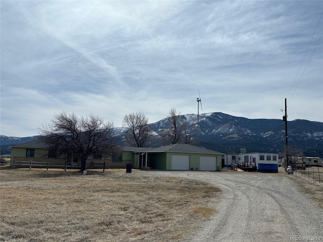 view of front of house with a garage, fence, a mountain view, and dirt driveway