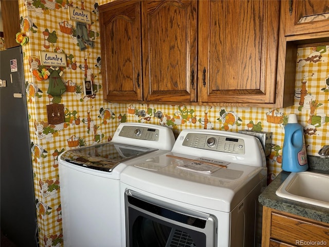 laundry room featuring wallpapered walls, a sink, cabinet space, and washer and clothes dryer