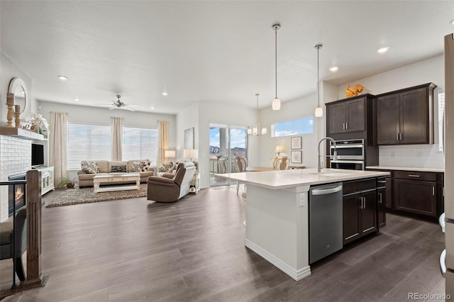 kitchen featuring dark hardwood / wood-style flooring, decorative light fixtures, a kitchen island with sink, and a brick fireplace