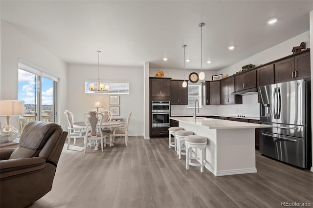 kitchen featuring hanging light fixtures, dark brown cabinets, stainless steel appliances, a center island with sink, and a kitchen bar