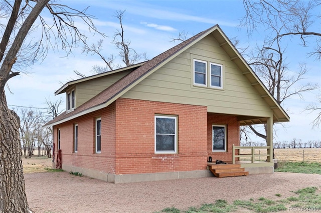 rear view of house with covered porch, brick siding, and roof with shingles