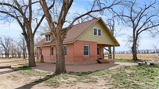 view of side of property featuring driveway, brick siding, and roof with shingles