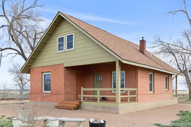 view of front of property with covered porch, brick siding, roof with shingles, and a chimney