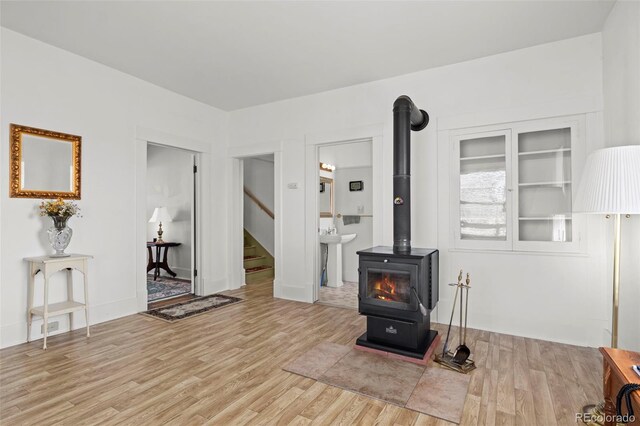 living area featuring light wood-style flooring, stairs, and a wood stove