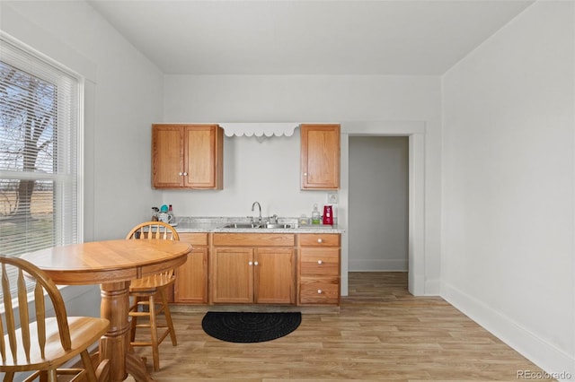 kitchen with light countertops, baseboards, a sink, light wood-type flooring, and brown cabinetry